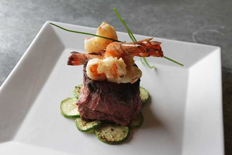 Steak topped with shrimp on top of a bed of cucumbers
